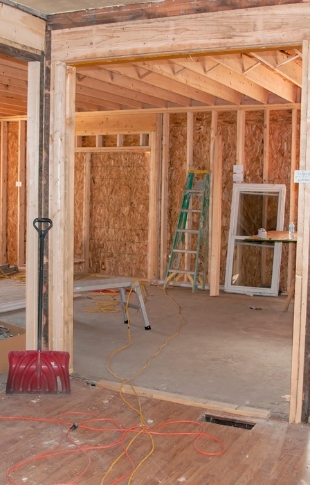 A wide view of an unfinished room addition to a home, including bare concrete floors, wall studs, and various equipment.