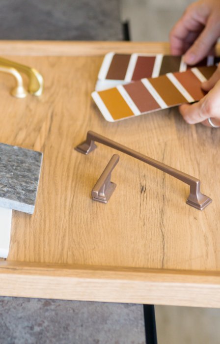 A close-up of a woman's hands holding a packet of designs next to a desk with color and material samples.