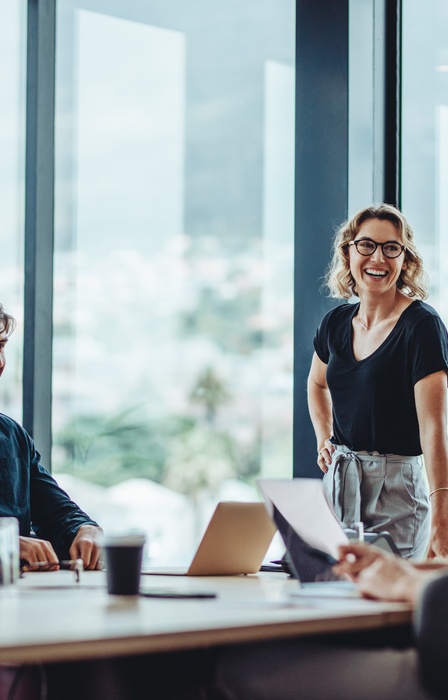 A manager and her employees smile and laugh together as they talk in a boardroom during a business meeting.