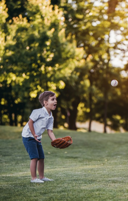 A man is kneeling on an open field. Several feet across from him is a child wearing a baseball glove.