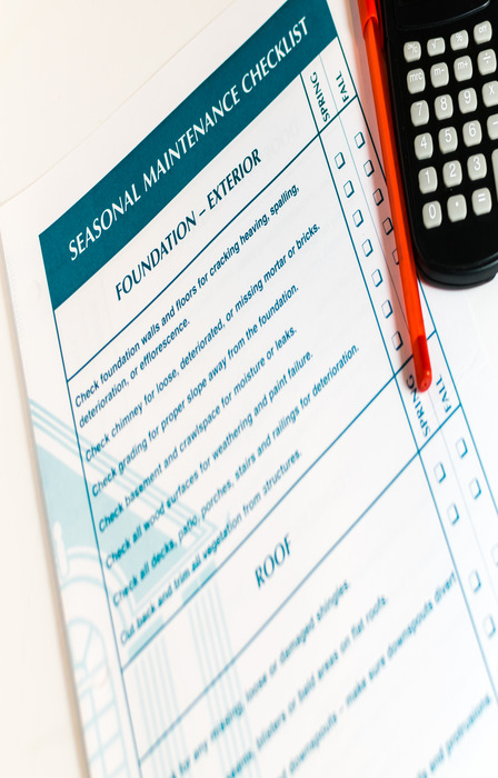 A document entitled "Seasonal Maintenance Checklist" next to a red pen and a calculator on a plain surface.