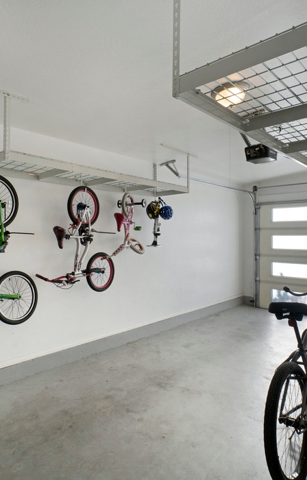 A clean and organized garage with white walls has three bikes hanging from bike hooks and four lined up on the ground.