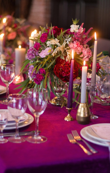 An elegant dining table with a hot pink tablecloth. Flowers, candles, and dinnerware line the table for an occasion.