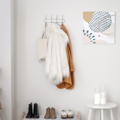 The entryway of a home with white walls, hooks holding jackets and purses, a shoe rack, and a white stool.