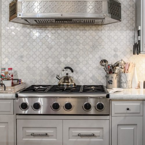 A contemporary home with a farmhouse kitchen with white cabinetry, a farmhouse sink, and a stainless steel stove and hood.