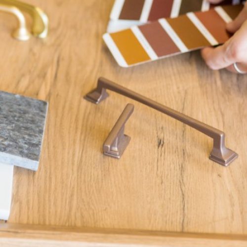 A close-up of a woman's hands holding a packet of designs next to a desk with color and material samples.