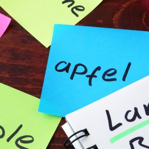 A notepad with the words "language barrier" written on it next to an apple. The word "apple" is written in four languages.
