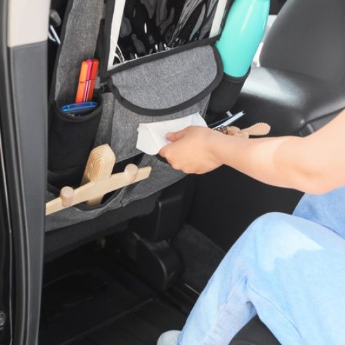 A person places an item into a car organizer attached to a front seat. The organizer holds a water bottle, tablet, and more.