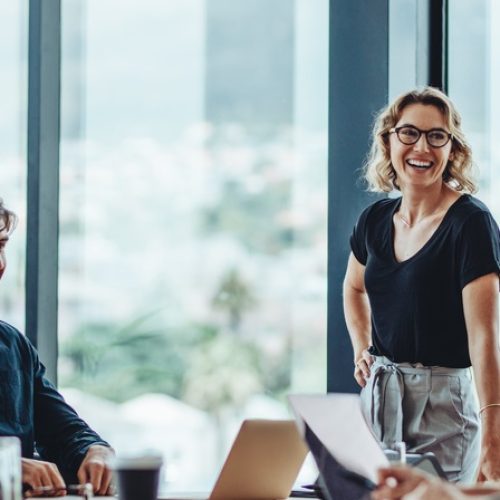 A manager and her employees smile and laugh together as they talk in a boardroom during a business meeting.