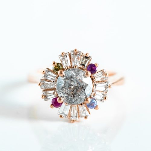 A close-up view shows a unique gold ring with a circular center diamond and baguette-shaped diamonds surrounding it.