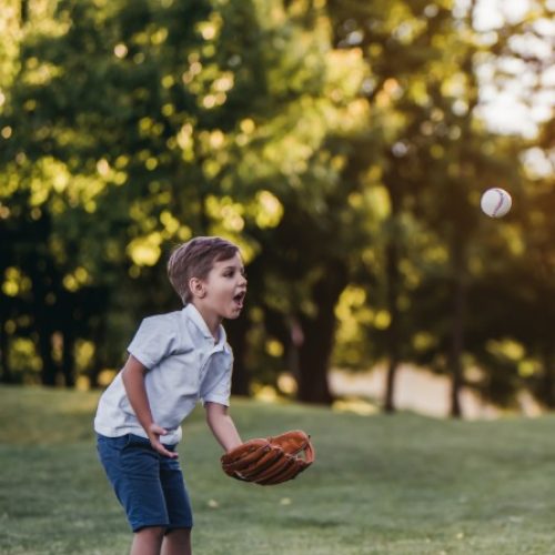 A man is kneeling on an open field. Several feet across from him is a child wearing a baseball glove.