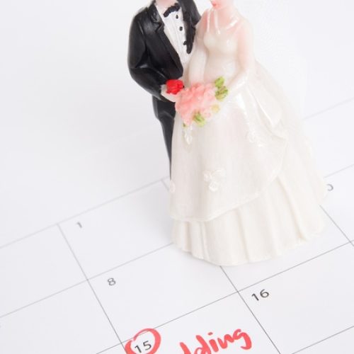 A figurine of a bride and groom on top of a calendar. The box for the 15th is circled in red and has "wedding" written inside.