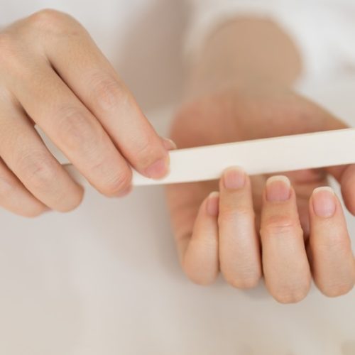 A close-up view shows a woman wearing a white shirt filing the nail on their ring finger with a white nail file.