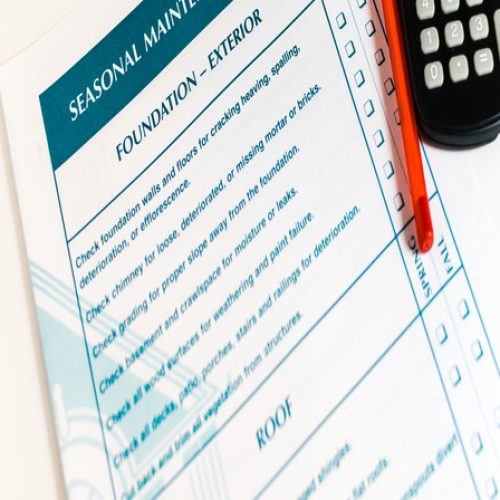 A document entitled "Seasonal Maintenance Checklist" next to a red pen and a calculator on a plain surface.