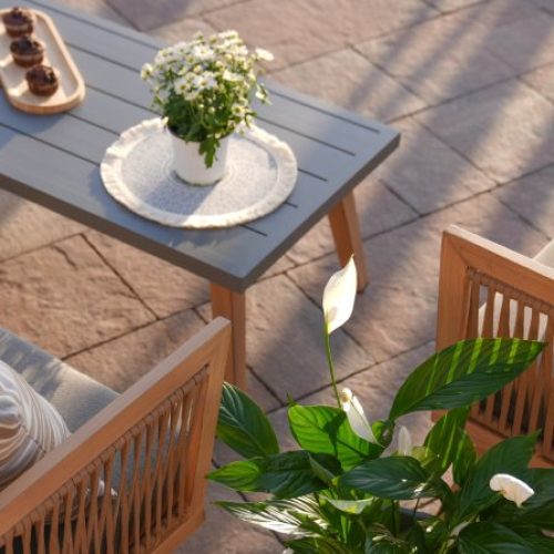 An overhead view of an outdoor patio space with garden tiles, a grey coffee table, and wooden chairs and loveseat.