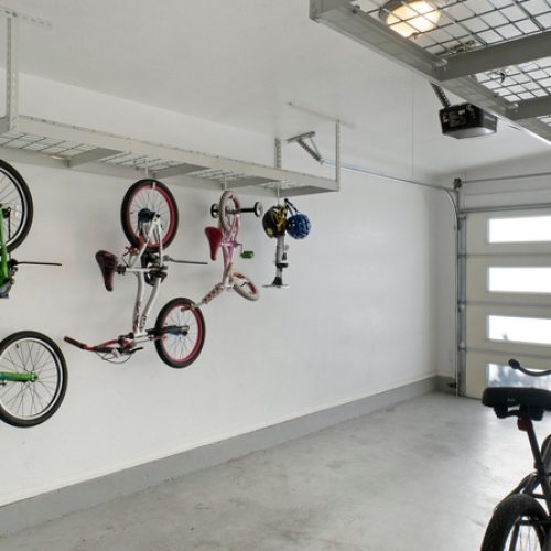 A clean and organized garage with white walls has three bikes hanging from bike hooks and four lined up on the ground.