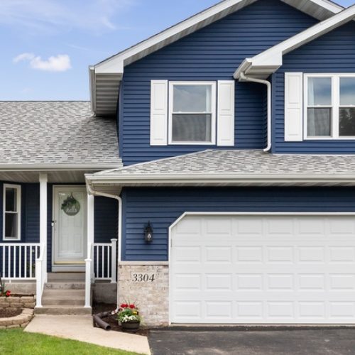 The exterior of a home with blue siding and gray roofs. All of the windows and doors are a bright white.