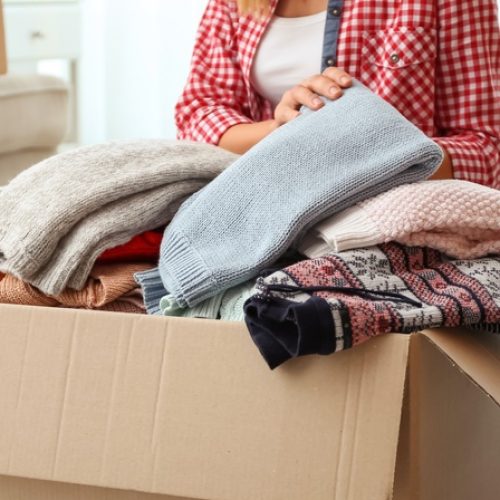 A woman sorts folded clothing into a cardboard donation box while another labeled donation box sits nearby.
