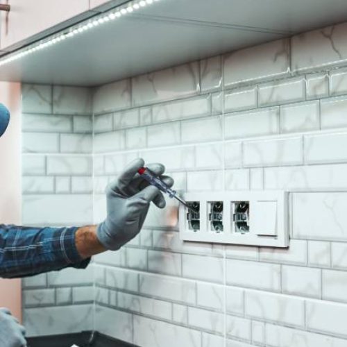 A professional handyman leans on the counter to fix issues with the electrical sockets on the backsplash area.