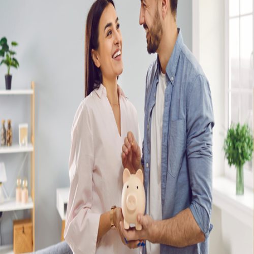 A couple smiles as they look at each other. They both hold a piggy bank, and the man goes to put money inside.