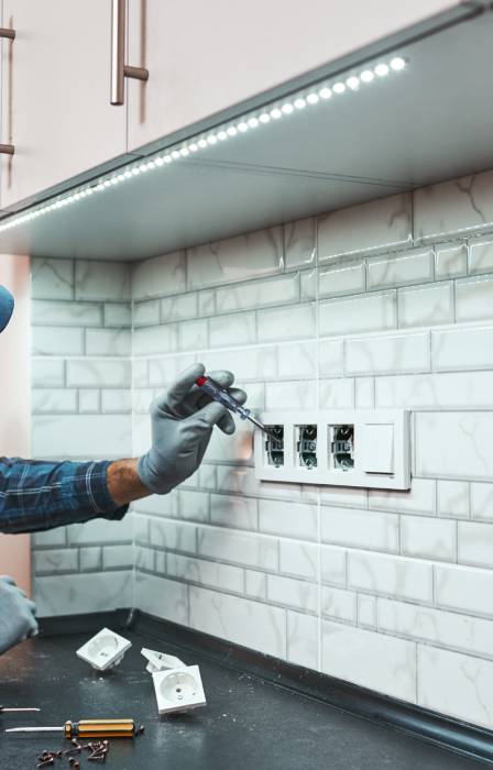 A professional handyman leans on the counter to fix issues with the electrical sockets on the backsplash area.